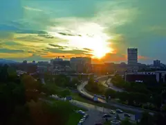 Панорама на София при залез с жилищни блокове, висока сграда с надпис GLOBUL, кран, пътни естакади и зеленина